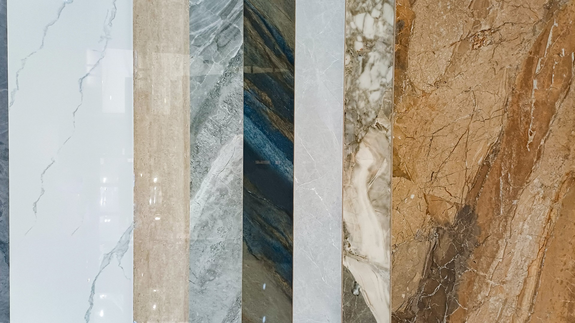 Vertical lineup of polished stone countertop slab samples — marble, granite, and quartzite — displayed for a Bucks County kitchen material selection appointment