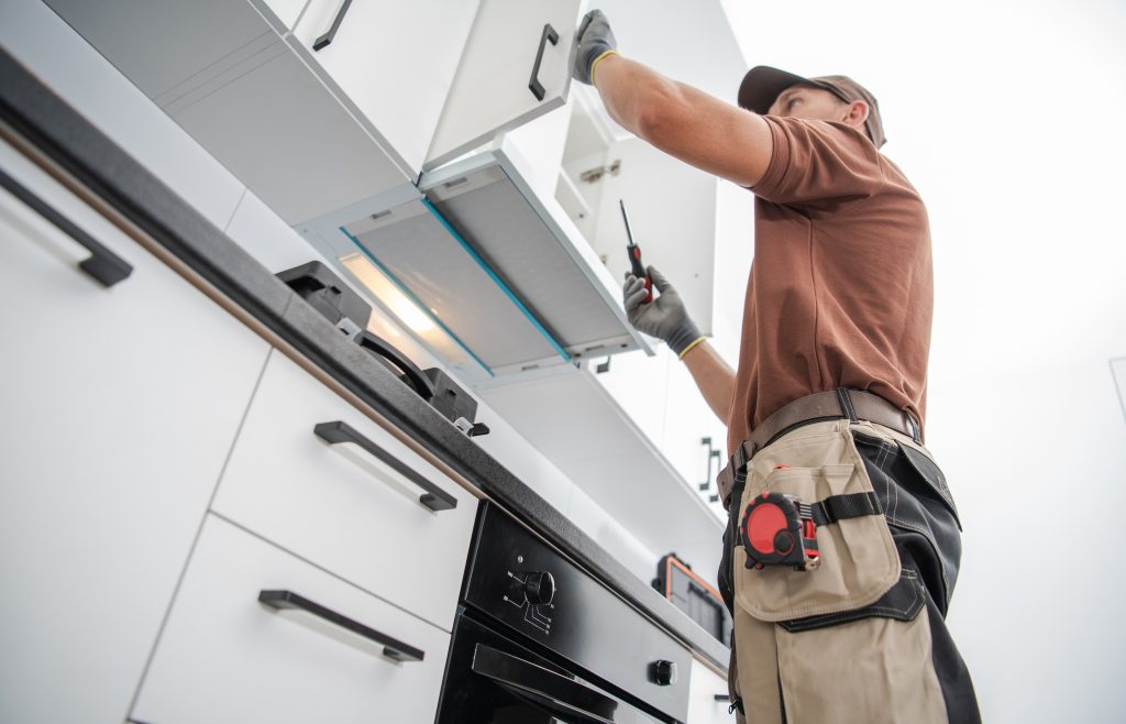 Installer in a tool belt fitting a wall cabinet and hood insert in a kitchen that is cabineted but not yet finished