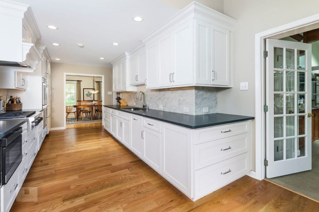 White kitchen wall cabinets carried all the way up to the ceiling with crown molding closing the joint, the soffit-free outcome
