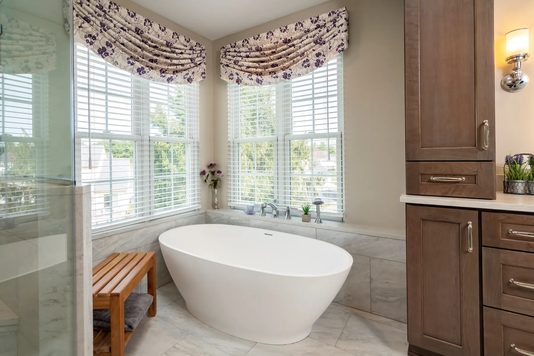 Remodeled bathroom with a freestanding soaking tub under bay windows and stained wood vanity cabinetry