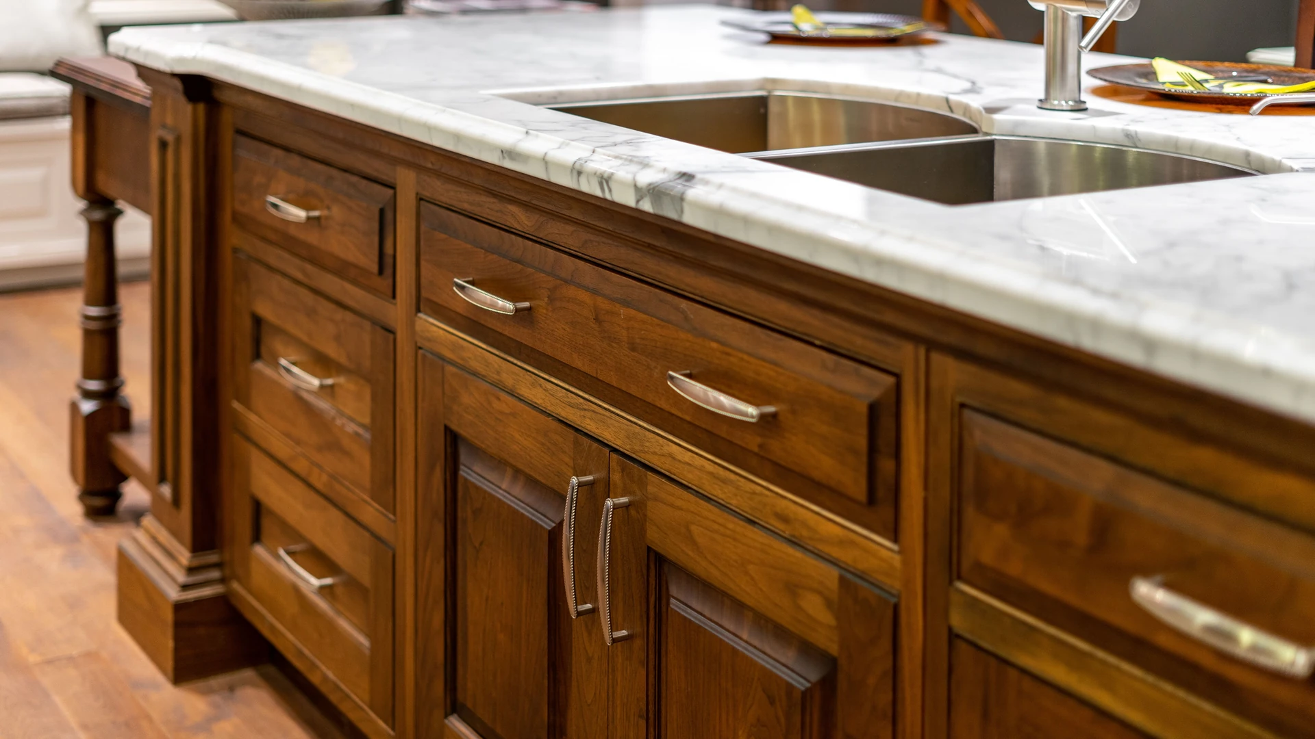 Dark brown kitchen island with paneled doors, drawers and metal pulls beneath a light veined countertop