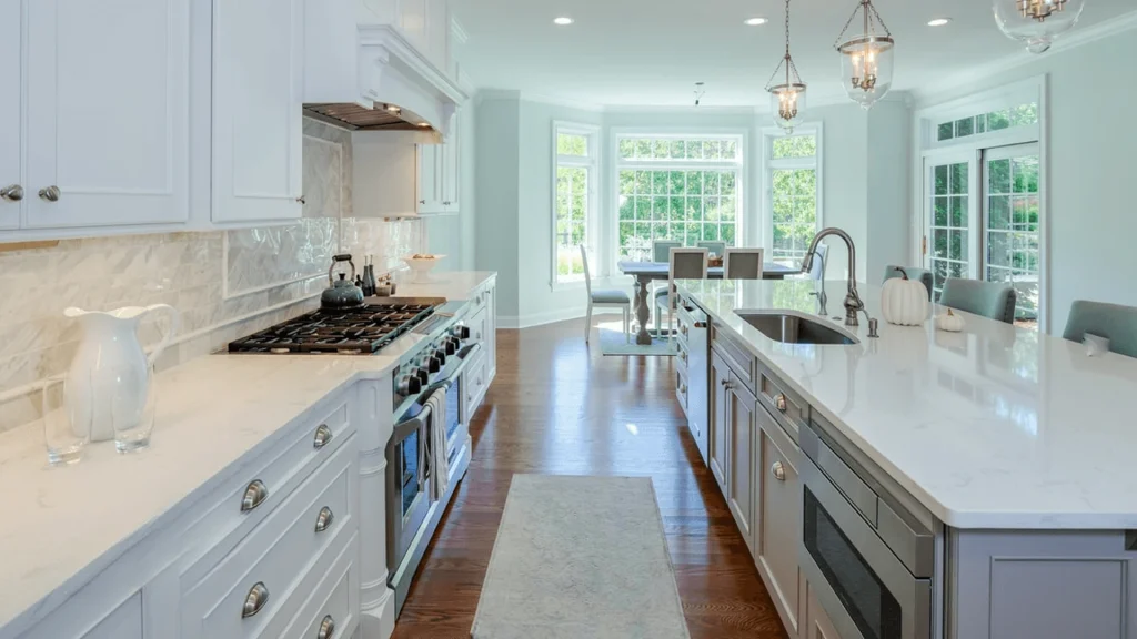 Galley kitchen with a range at left and an island at right holding a sink and a stainless-steel microwave drawer in its base cabinetry, with a dining nook in the background