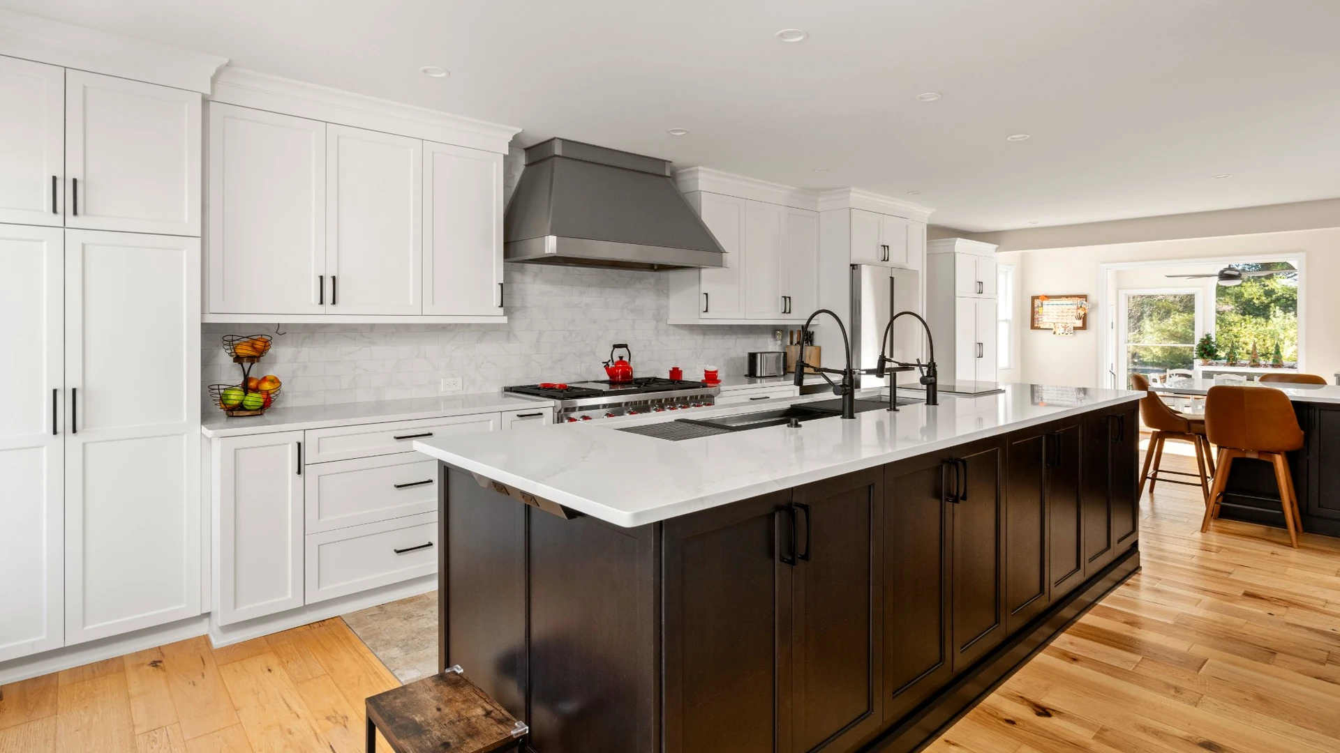 Open kitchen with white shaker cabinets, a long dark island with white countertop and a metal range hood
