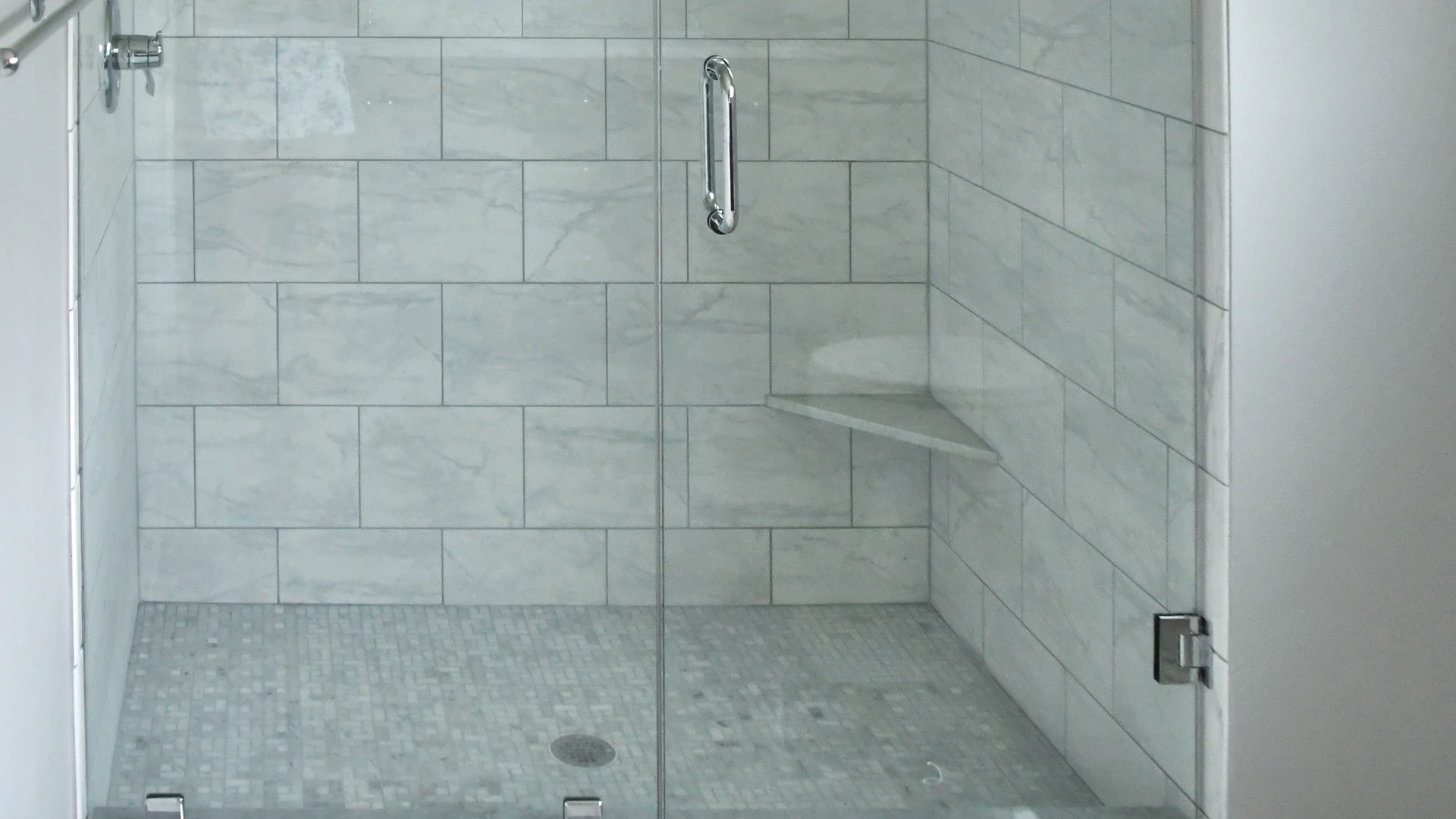 Walk-in glass shower with marble-look subway tile and a built-in triangular corner bench seat