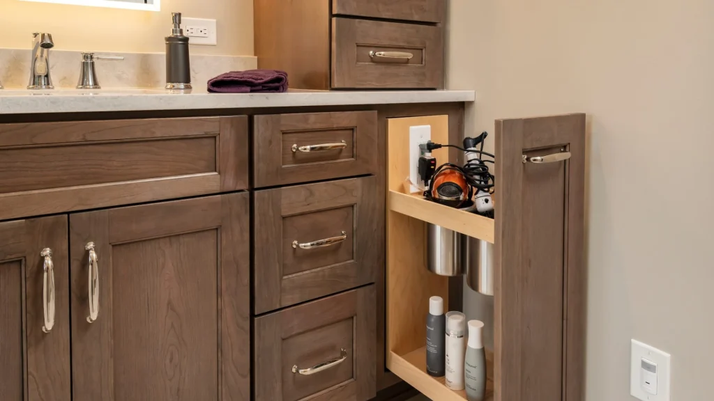A vanity pullout cabinet drawn open, with a hair dryer plugged into a receptacle on its inside wall, a wall receptacle above the counter beside the soap dispenser, and a wall-mounted occupancy sensor at the right edge