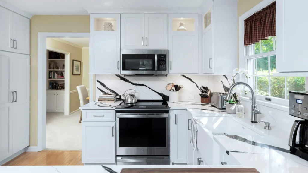 White backsplash with bold black veining extends from the countertop to the wall cabinets behind a silver-colored range and microwave, and to the window sill beside the sink.